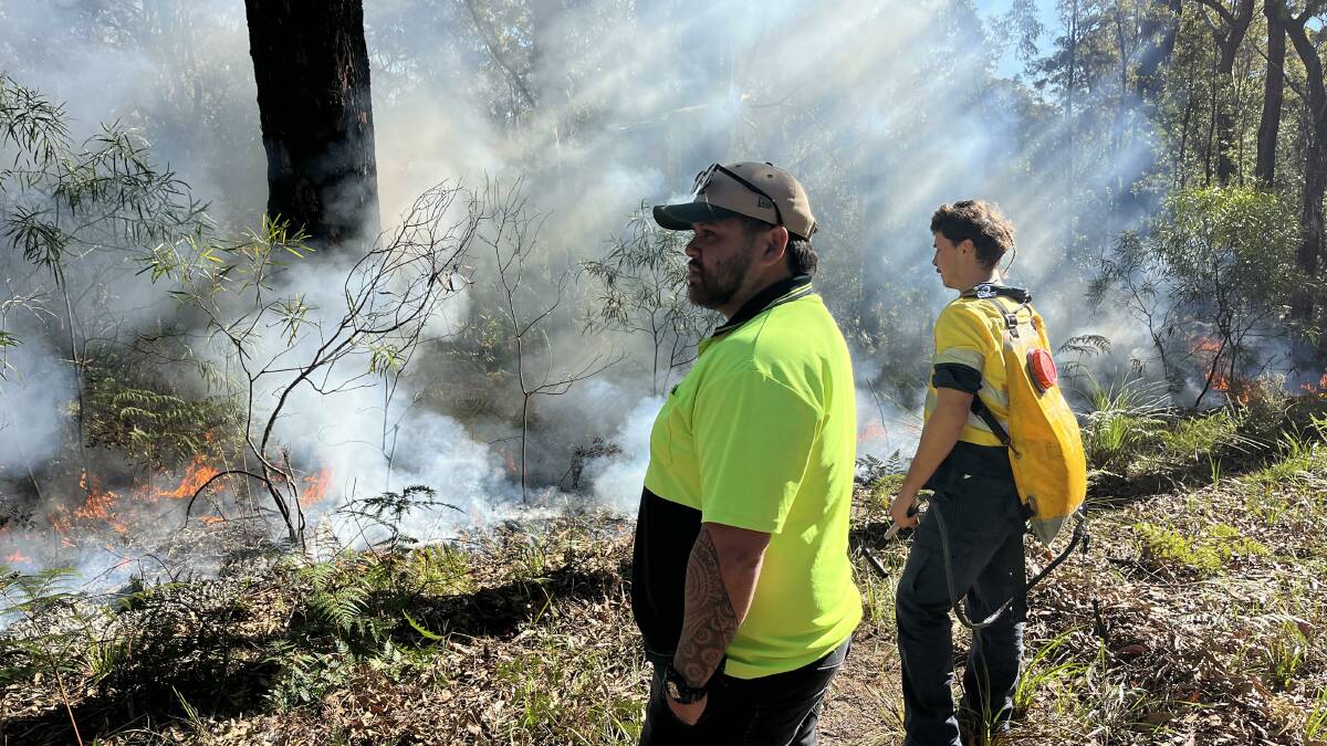 Two men watch the landscape as the fire reduces the scrub on the ground. Picture by James Parker